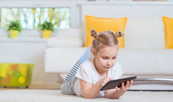 Mooi klein meisje met behulp van een digitaal tablet, op zoek en glimlachen — Stockfoto