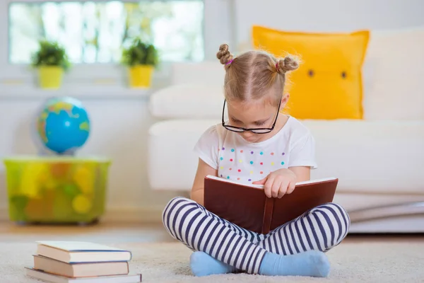 Porträtt av smart liten flicka sitter med boken på golvet — Stockfoto