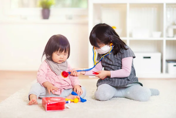 Dos feliz japonés hermanas jugando con médico conjunto en casa — Foto de Stock