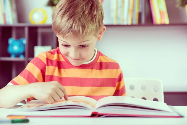 Menino da escola primária na mesa lendo boock — Fotografia de Stock