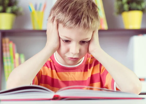 Хлопчик початкової школи за столом читає бут — стокове фото