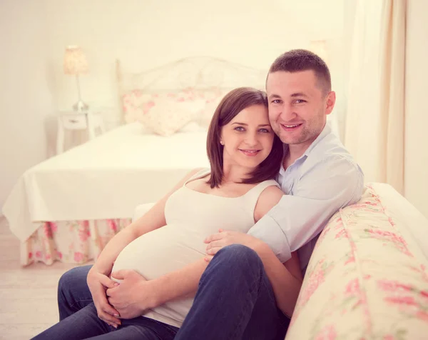 Счастливая беременная пара на диване — стоковое фото