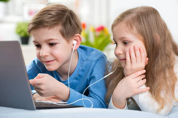 Dos niños felices jugando con el ordenador portátil y escuchando música con —  Fotos de Stock