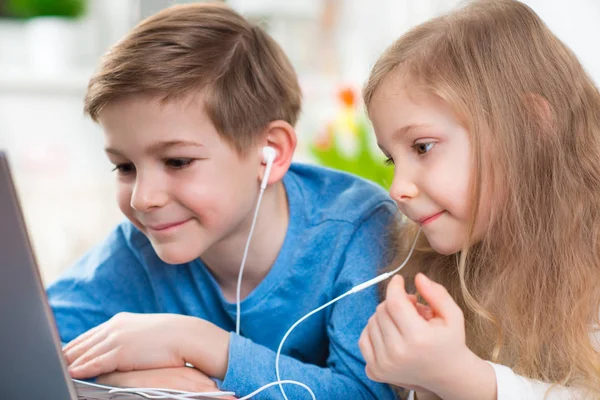 Dos niños felices jugando con el ordenador portátil y escuchando música con —  Fotos de Stock