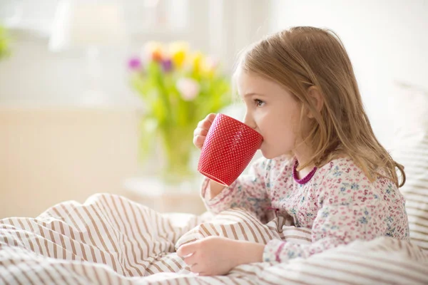 Ganska sjukt liten barn flicka i sängen dricka te — Stockfoto