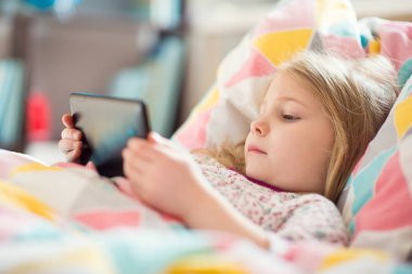 Küçük kız yatakta tablet ile oynamak