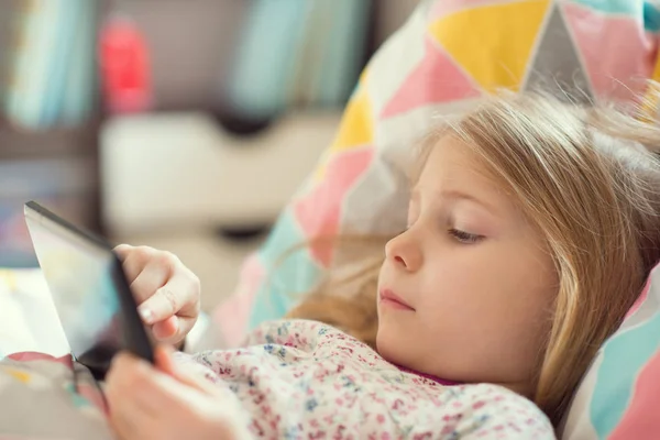 小さな女の子がベッドでタブレットで遊んで — ストック写真