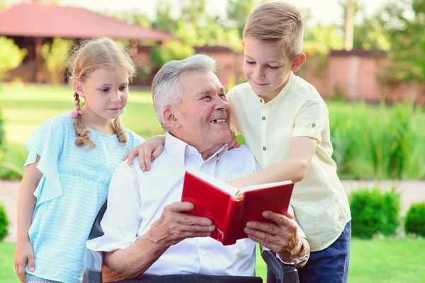 Šťastné staré dědeček čtení knihy pro roztomilé děti v zahradě — Stock fotografie