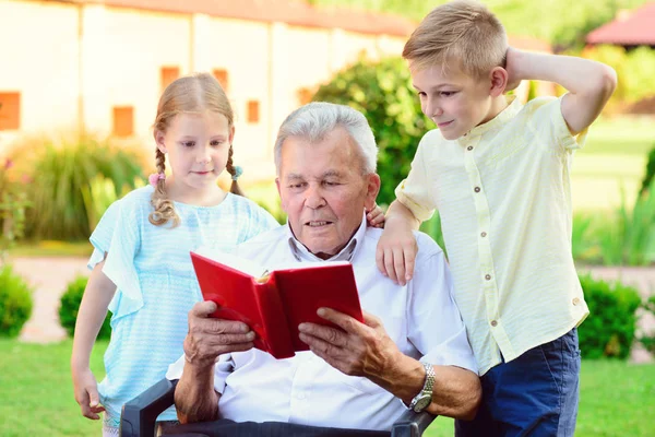 Feliz velho avô ler livro para crianças bonitos no jardim — Fotografia de Stock