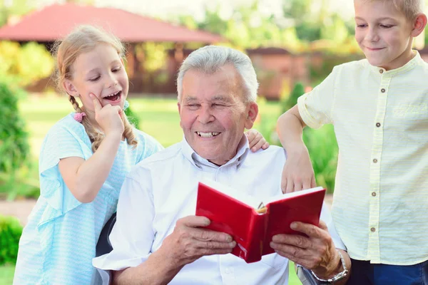 Happy old grandfather reading book for cute children  in garden — Stock Photo, Image