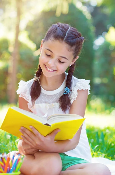 Porträtt av ganska ung flicka läsebok i park — Stockfoto