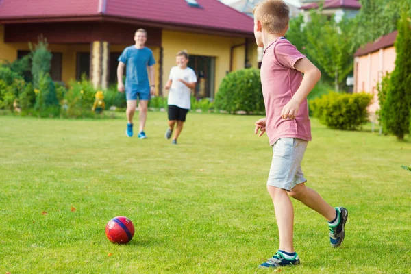 Deux fils heureux jouant au football avec leur père dans le jardin près — Photo