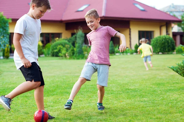 Dois filhos felizes jogando futebol com seu pai no jardim perto — Fotografia de Stock