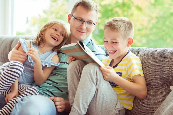 Joven padre feliz leyendo libro con niños lindos en casa —  Fotos de Stock