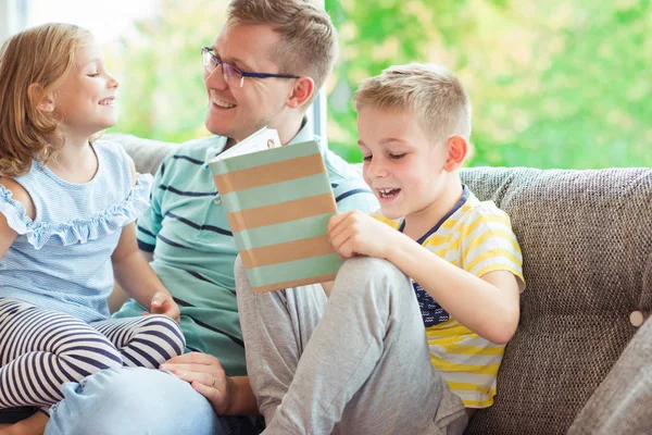 Young happy father reading book with cute children at home — Stock Photo, Image