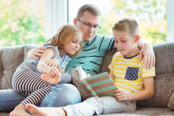 Junger glücklicher Vater liest Buch mit niedlichen Kindern zu Hause — Stockfoto