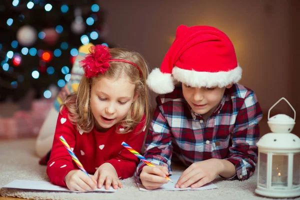 Duas crianças felizes escrevendo carta para o Papai Noel em casa perto de Ne — Fotografia de Stock
