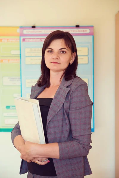 Pretty young teacher is standing with book near blackboard — Stock Photo, Image