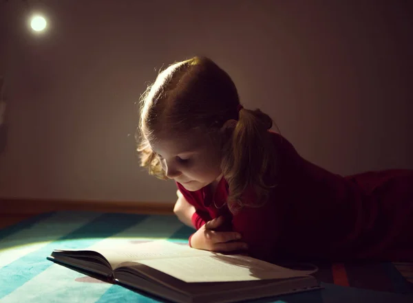 Hübsches kleines Mädchen liest Buch in ihrem Versteck mit Flashli — Stockfoto