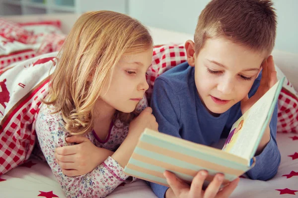 Двоє щасливих дітей-братів читають книгу в двоярусному ліжку під ковдрою — стокове фото