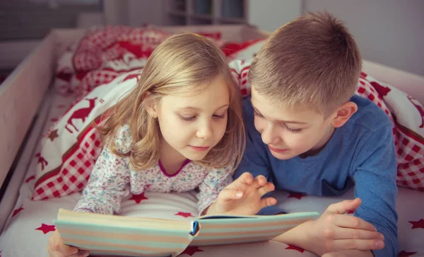Dos niños felices hermanos leyendo libro en litera bajo blanke — Foto de Stock