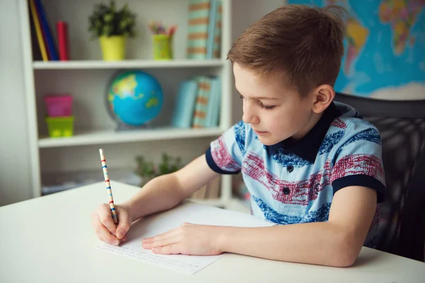 小聪明的学校男孩做家庭作业在书桌在房间里 — 图库照片