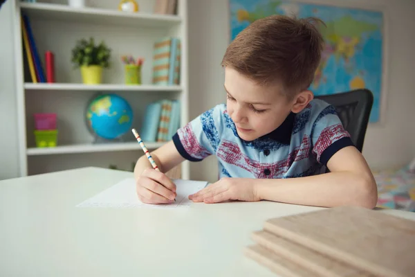 Petit écolier intelligent faisant ses devoirs au bureau dans la chambre — Photo