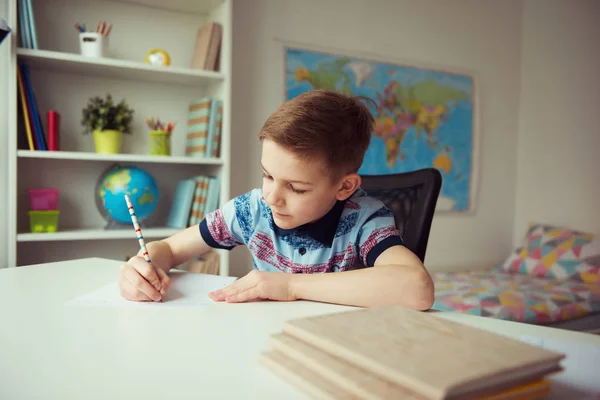 Liten smart skola pojke att göra läxor på skrivbord i rummet — Stockfoto