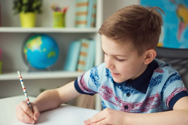 Malý chlapec chytrý školy dělat domácí úkoly u stolu v pokoji — Stock fotografie