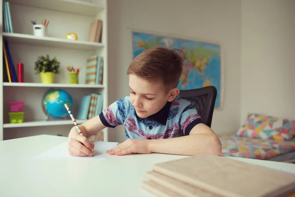 Liten smart skola pojke att göra läxor på skrivbord i rummet — Stockfoto