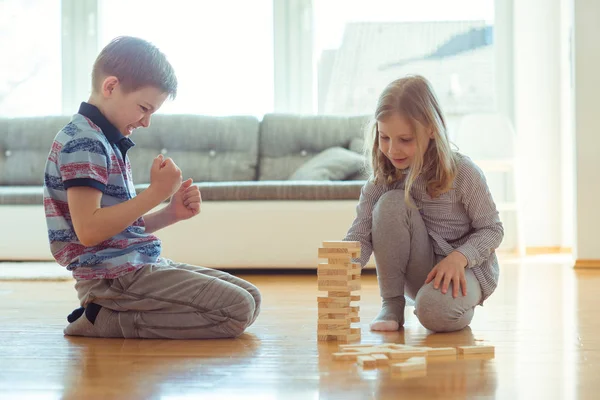 Двое счастливых братьев и сестер играют в игру с деревянными блоками дома — стоковое фото