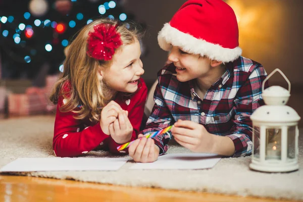 Dos niños felices escribiendo una carta a Santa Claus en casa cerca de Ne —  Fotos de Stock