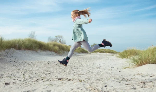 Glückliches kleines Mädchen im blauen Kleid springt an einem sonnigen Tag am Strand — Stockfoto