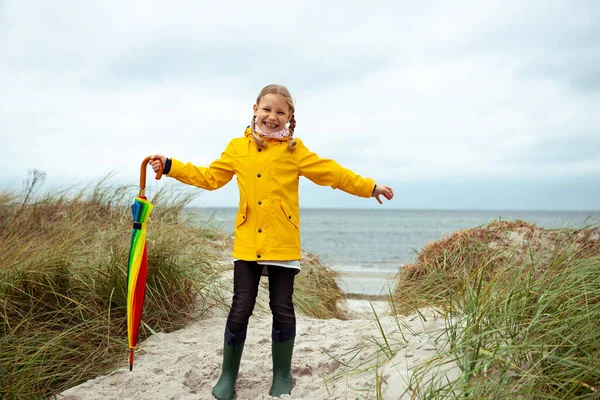 Fröhliches kleines Mädchen am Strand mit buntem Sonnenschirm auf — Stockfoto