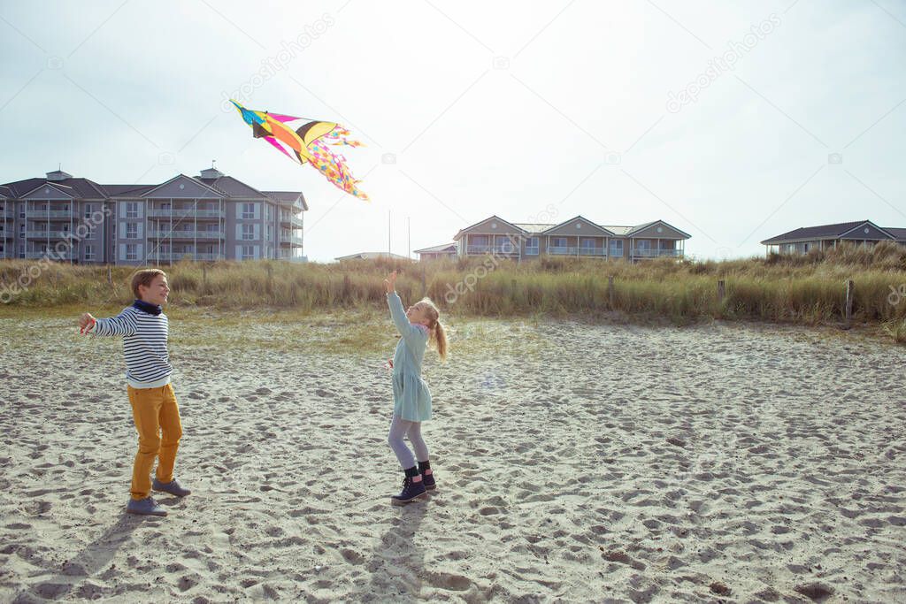 Happy siblings children running and having fun with kite on beac