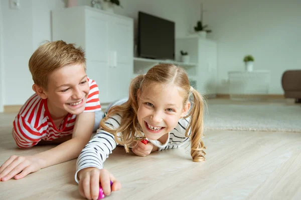 Portret van twee vrolijke kinderen die op de vloer liggen en spelen — Stockfoto