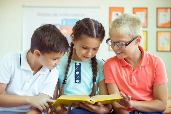 Gelukkige basisstudenten zitten op bureau met boek en discussie — Stockfoto