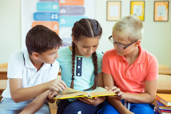 Gelukkige basisstudenten zitten op bureau met boek en discussie — Stockfoto