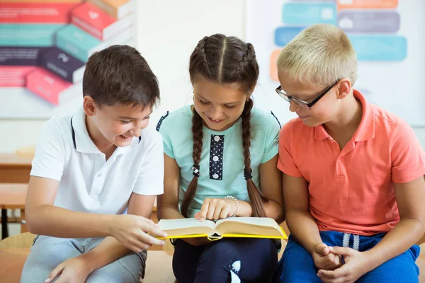 Happy elementary students sitting on desk with book and discussi — Stock Photo, Image