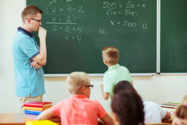 Genç erkek öğretmen matematik dersini karatahtada anlatıyordu.