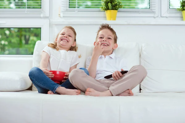 Маленькие брат и сестра смотрят телевизор на диване — стоковое фото