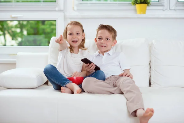 Маленькие брат и сестра смотрят телевизор на диване — стоковое фото