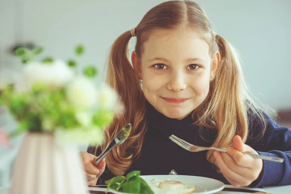 Linda chica adolescente rubia comiendo huevos benedicto con cuchillo y tenedor —  Fotos de Stock