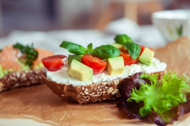 Tam tahıllı tost, avokado, domates ve somon, kafeteryada ahşap kesim tahtasında.