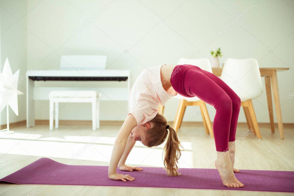 Pretty happy child girl having fun making yoga exercises at home during coronavirus quarantine