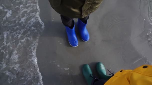两个孩子穿着色彩艳丽的橡胶高跟鞋站在冰冷的波罗的海的水里 — 图库视频影像