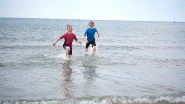 ビーチで実行され 波と砂で遊ぶネオプレン水着で2人の幸せな子供のスローモーションビデオ — ストック動画