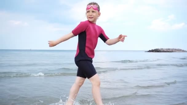 ビーチで実行され 波と砂で遊ぶネオプレン水着でかなり幸せな女の子のスローモーションビデオ — ストック動画