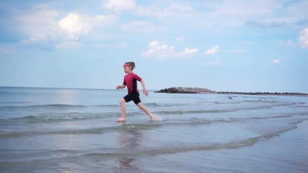 네오프렌 수영복을 해변을 뛰어다니며 파도와 속에서 소녀의 비디오 — 비디오