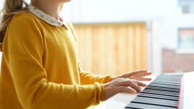 Evde modern beyaz e-piyanoda piyano dersi alan küçük güzel bir kızın portresi.